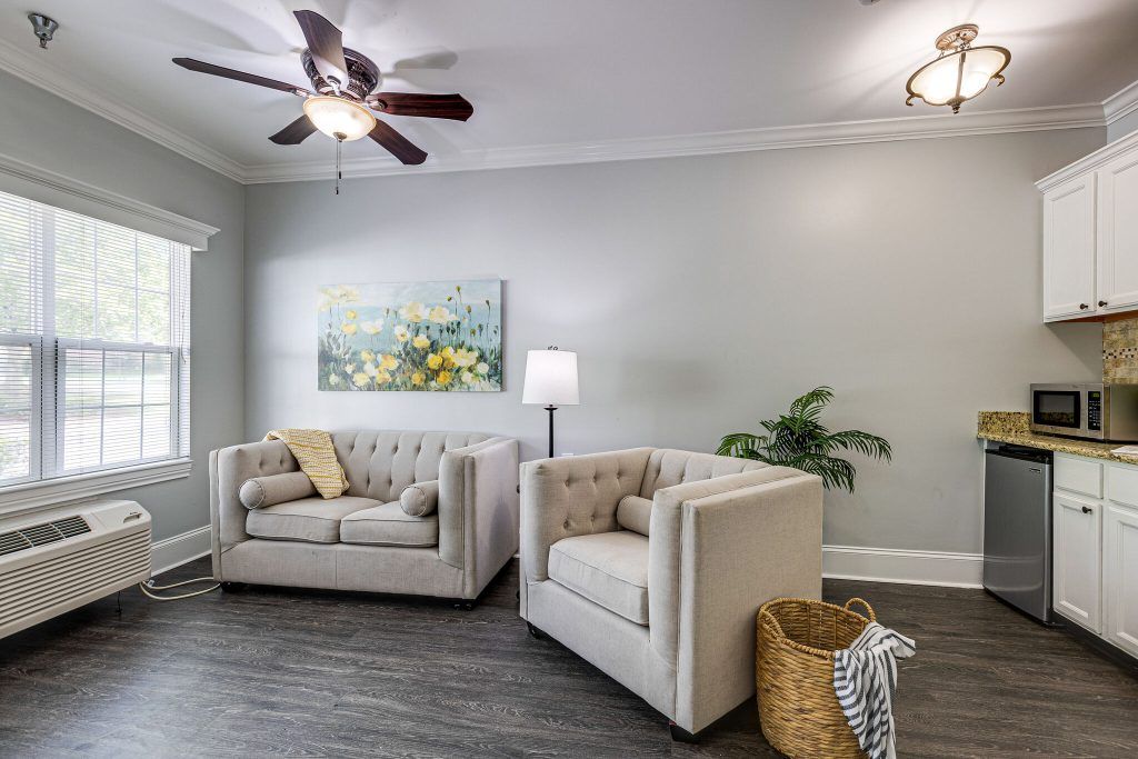 A modern living room with two armchairs, a floor lamp, and wall art, featuring a ceiling fan and cozy decor.