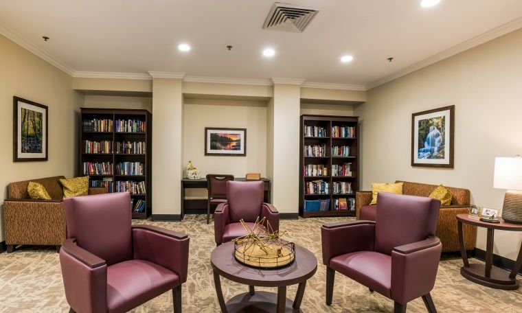 A cozy reading room with bookshelves and comfortable chairs, featuring a chess board in the center.