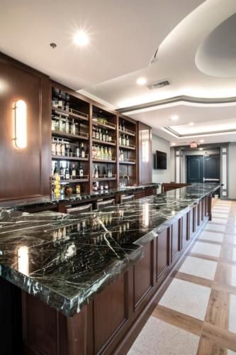 A luxurious bar interior with a sleek countertop and wooden shelves lined with bottles.