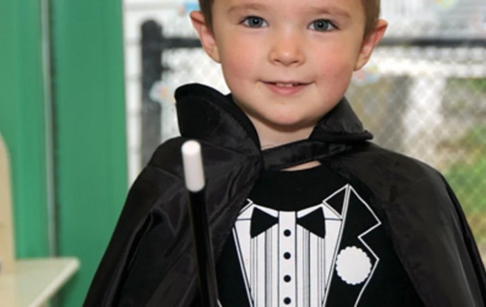 A young child dressed as a magician, complete with a black cape and wand.