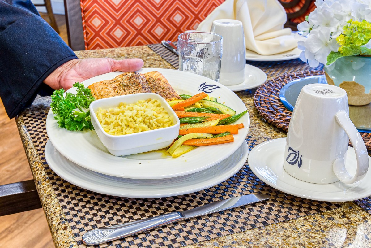 A beautifully arranged plate of salmon, vegetables, and corn served at a restaurant table.