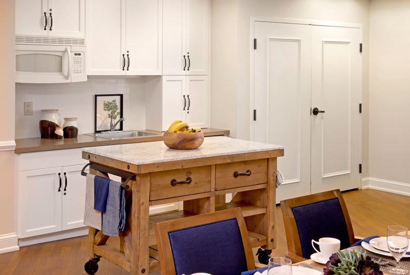 A cozy kitchen featuring a wooden island with a fruit bowl and white cabinetry.