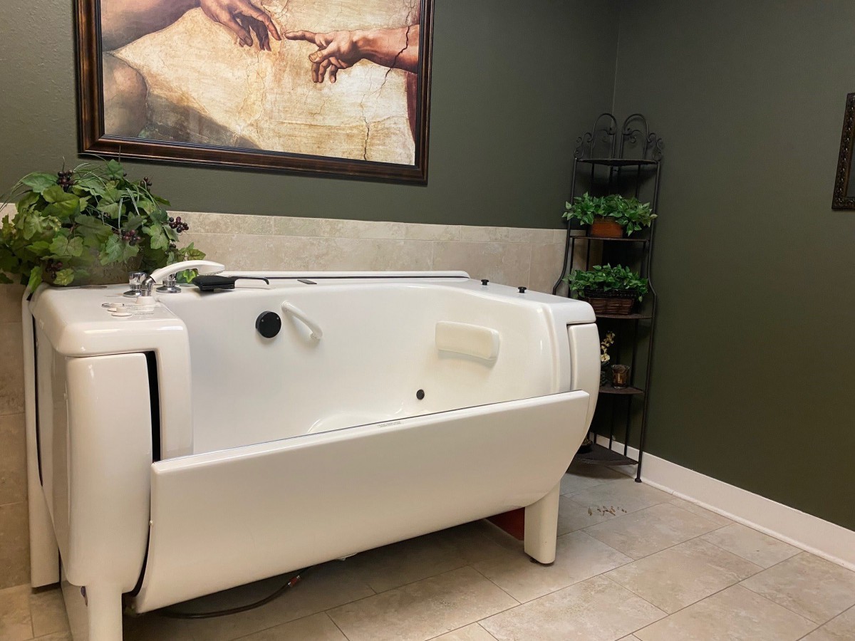 A modern bathroom with a white bathtub and green walls, featuring artwork and plants for decor.