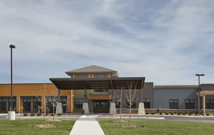 A modern building with a prominent entrance and a walkway leading to it, set against a partly cloudy sky.