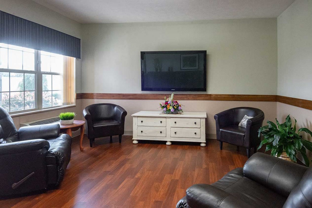 A cozy living room with leather chairs, a large television, and a white console on hardwood flooring.
