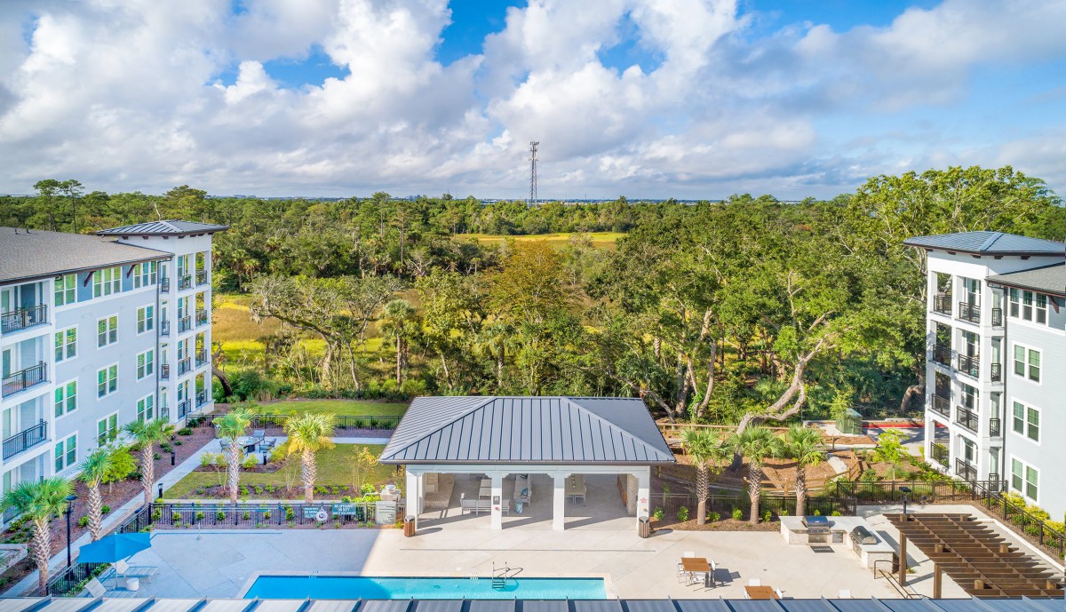 A modern house with a pool surrounded by lush greenery and a scenic landscape under a partly cloudy sky.