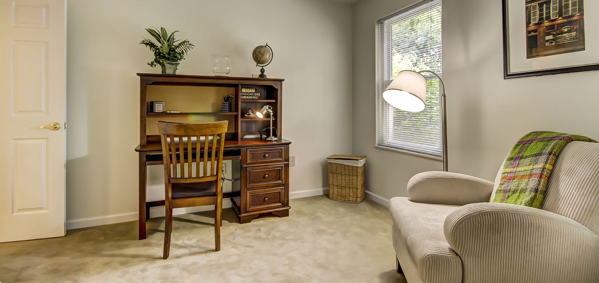 A cozy home office with a wooden desk, chair, and globe, illuminated by natural light from a window.