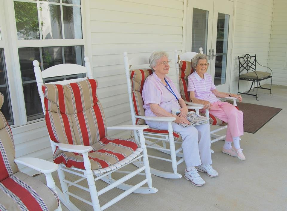 Two elderly individuals sitting on rocking chairs on a porch.