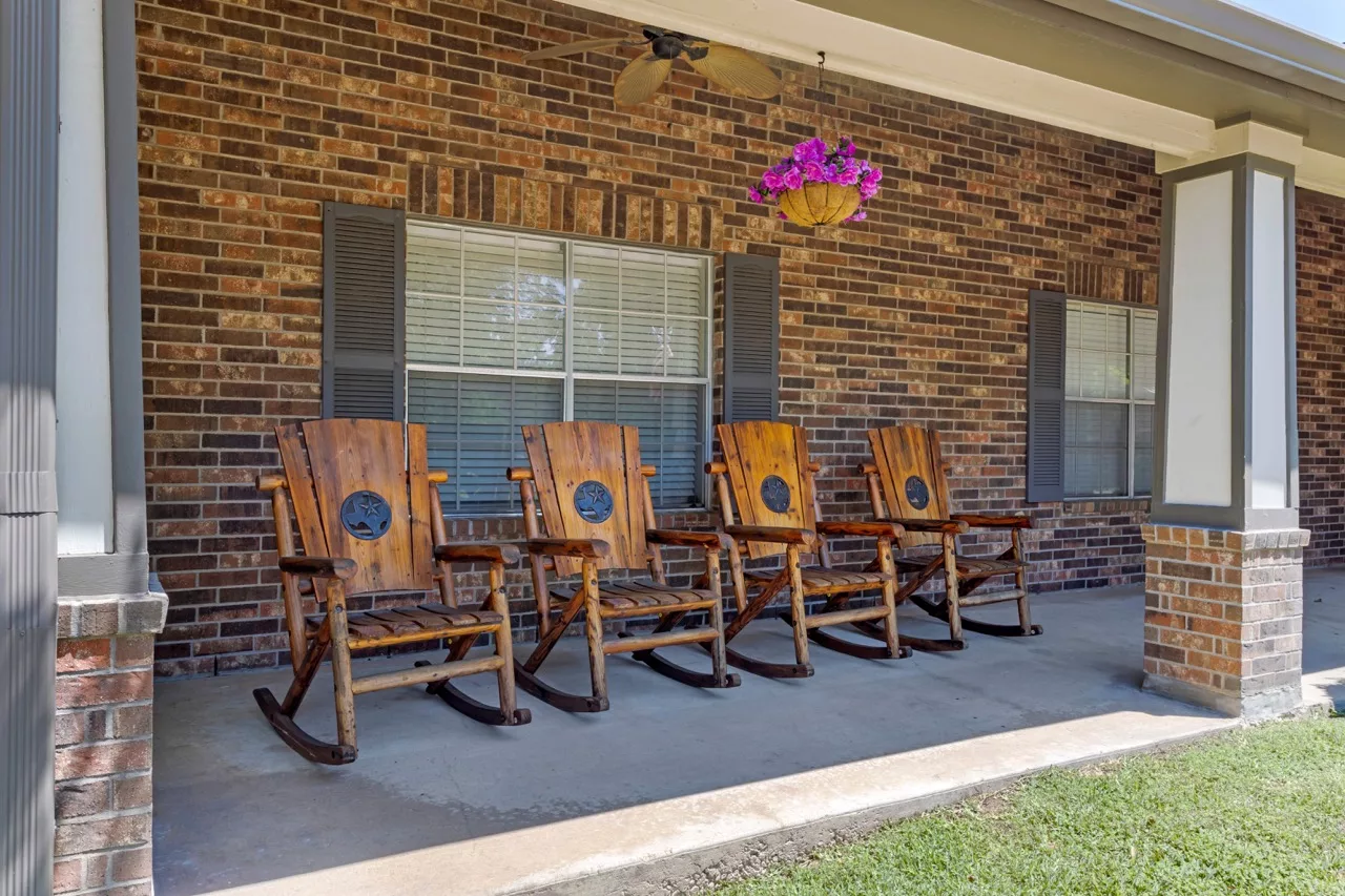 A row of wooden rocking chairs on a porch with a hanging plant above.