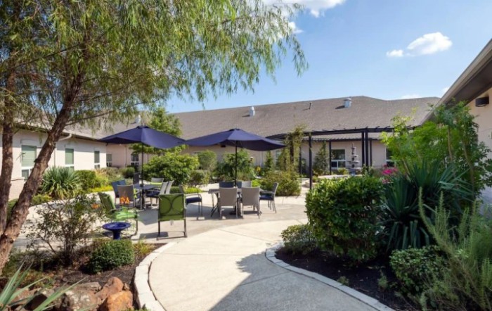A serene garden patio with outdoor seating, umbrellas, and lush greenery.