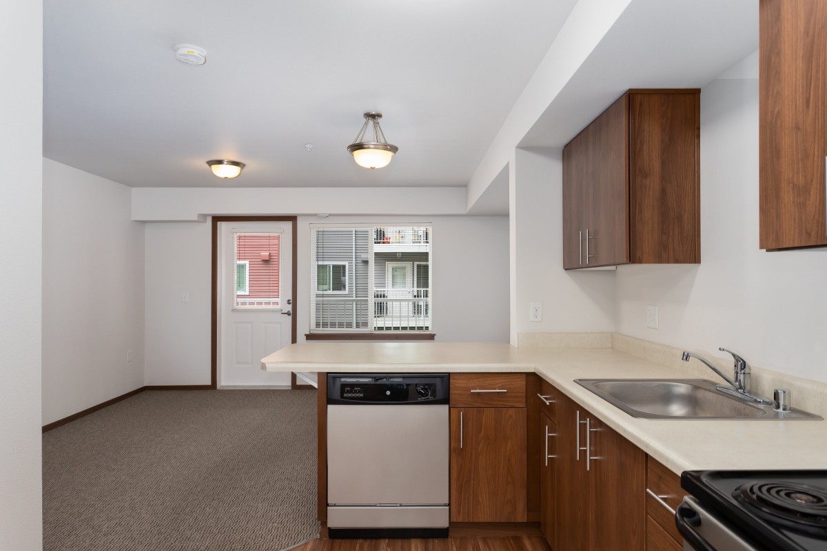 A modern apartment kitchen with wooden cabinets and stainless steel appliances.