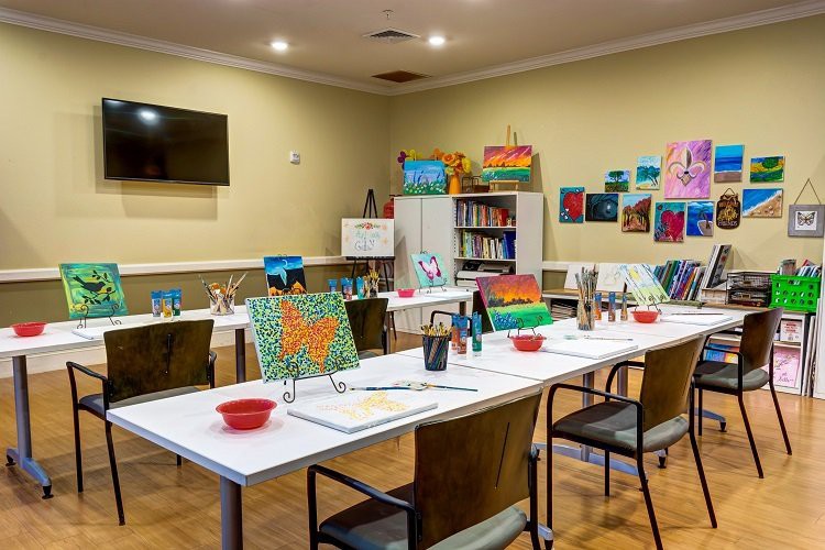 A well-equipped art studio set up for a painting class, featuring tables with supplies and colorful artwork on display.