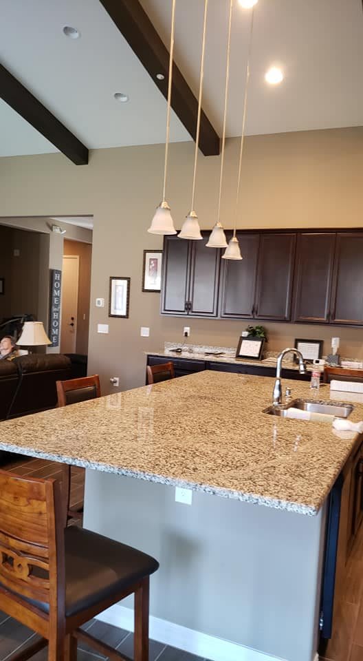 A modern kitchen featuring a large granite countertop island with pendant lighting and dark wood cabinets.