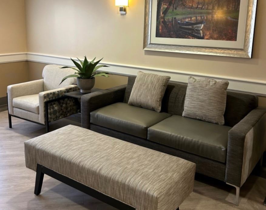 A cozy living room setup featuring a sofa, armchair, and coffee table with decorative elements like a potted plant and a framed painting on the wall.