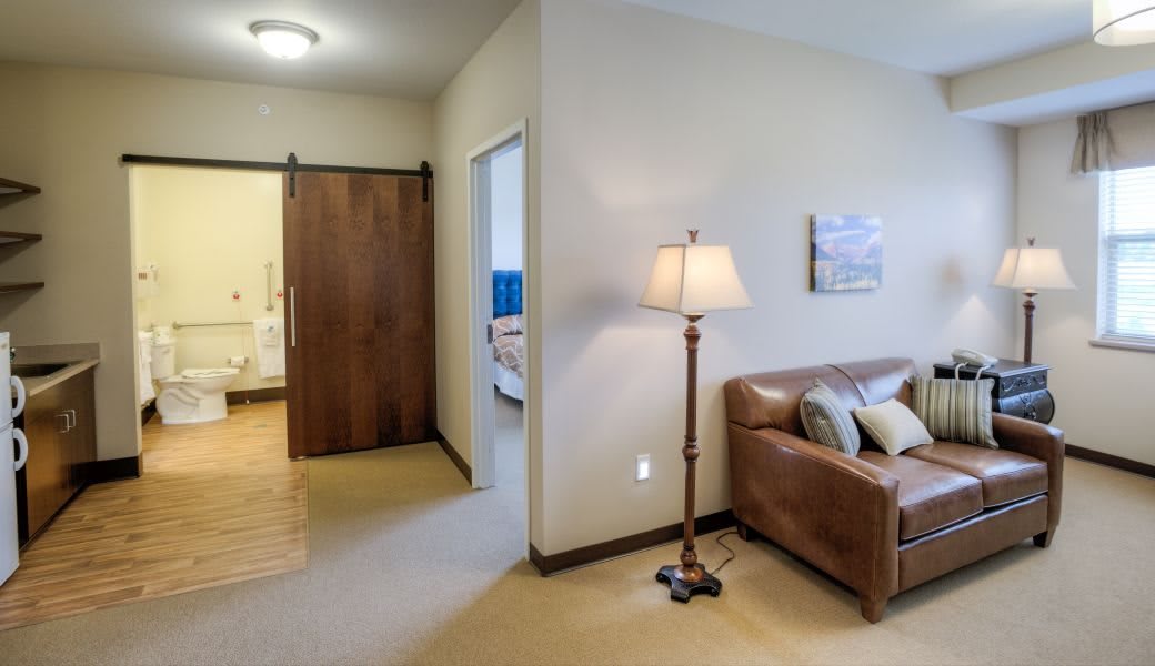 A cozy living room area with a sofa and a floor lamp, adjacent to a hallway leading to another room.