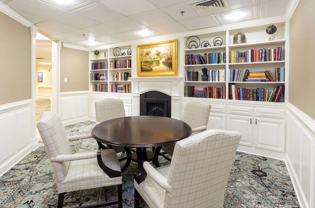 A cozy library room with a round table and upholstered chairs surrounded by bookshelves.