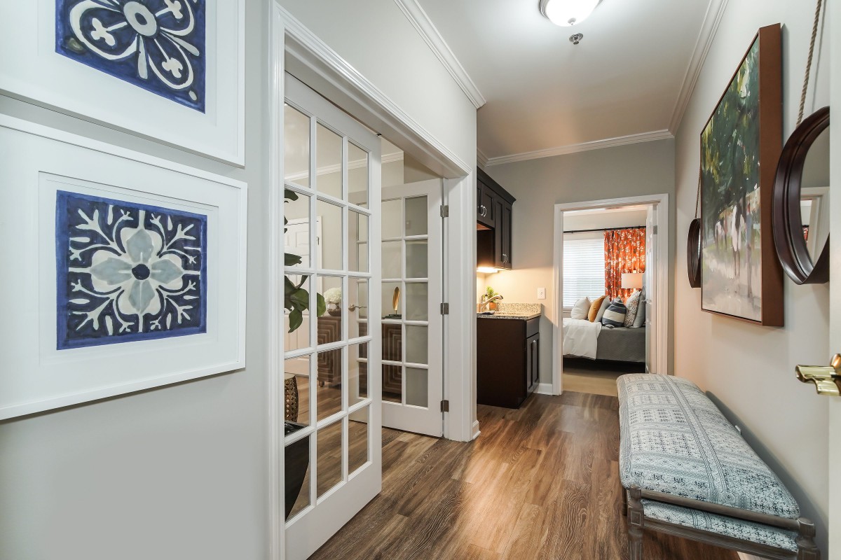 A modern hallway with wood flooring, featuring French doors, artwork on the walls, and elegant lighting.