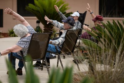 A group of seniors participating in an outdoor exercise session while seated in chairs.