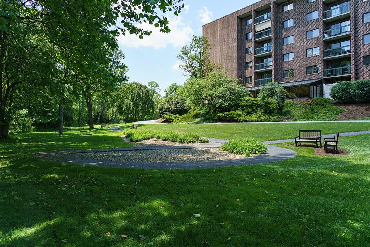 A serene park area with lush greenery and a modern apartment building in the background.