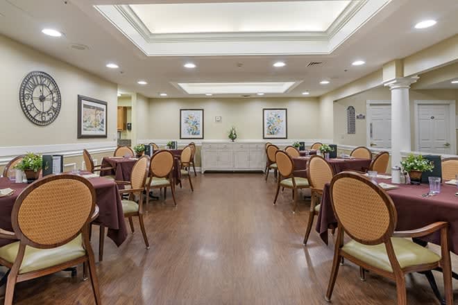 A restaurant dining room with neatly arranged tables and chairs, decorated with artwork on the walls and illuminated by ceiling lights.