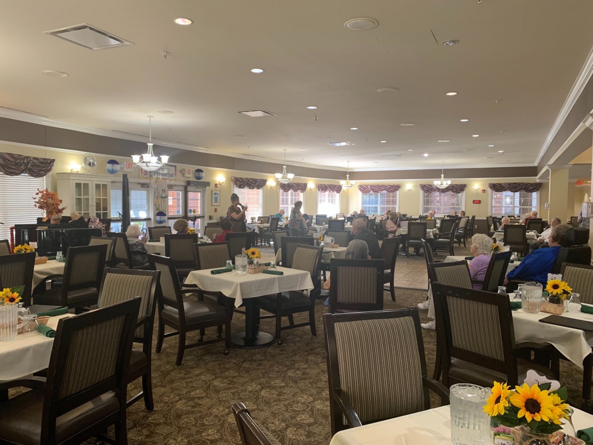 A spacious dining hall with tables and chairs, occupied by people gathered for a meal.