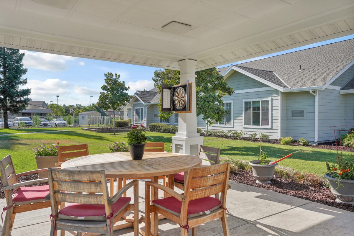 A cozy outdoor patio area with a wooden table and chairs, surrounded by well-maintained gardens.