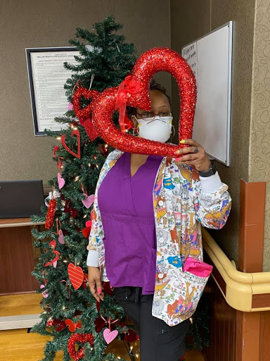 A cheerful staff member celebrating the holiday season with festive decorations and a heart-shaped prop.