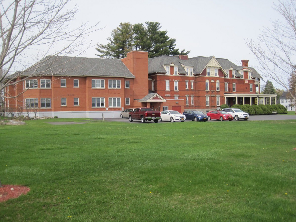 A historic brick building with a well-maintained lawn and parked cars in front.