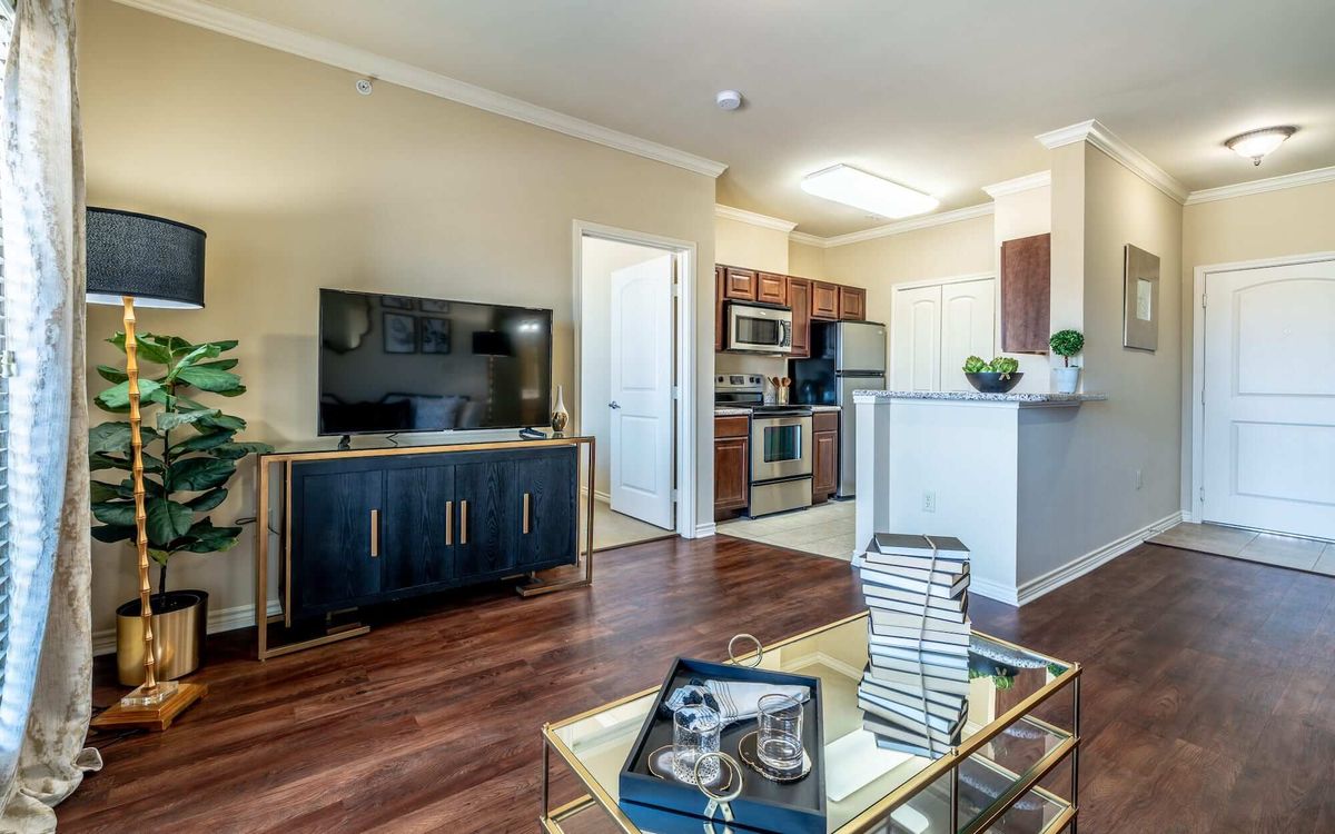 A cozy living room with a television, modern furnishings, and an open kitchen layout.