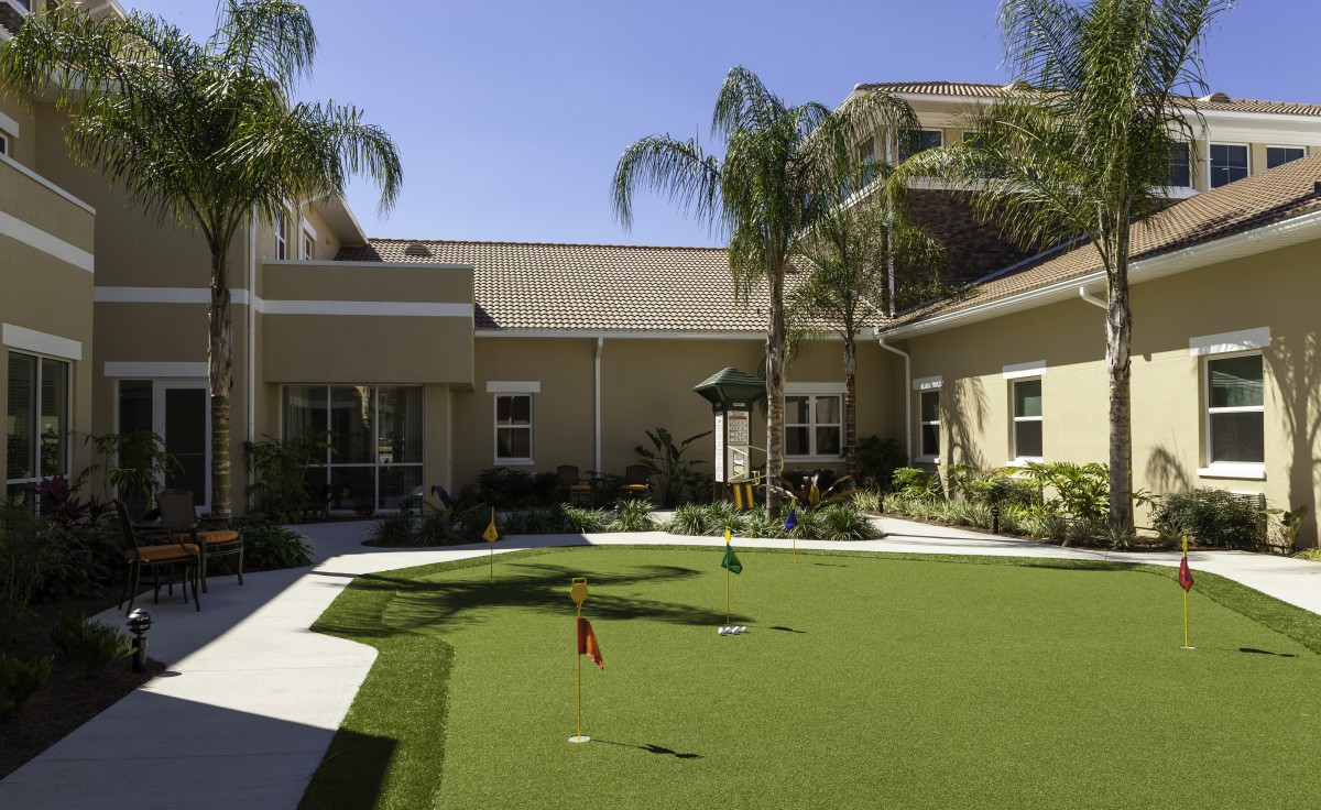 A sunny courtyard with a putting green surrounded by palm trees and buildings.