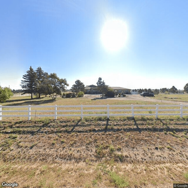 A sunny rural landscape with a white fence and trees in the distance.