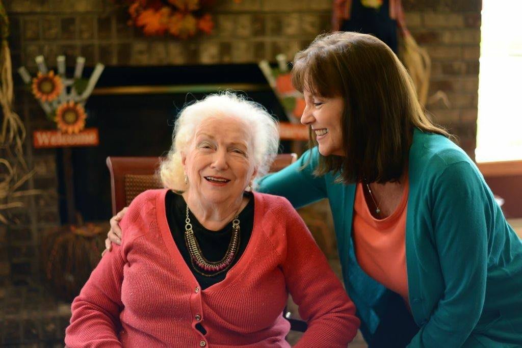 An elderly woman and a younger woman share a joyful moment indoors.