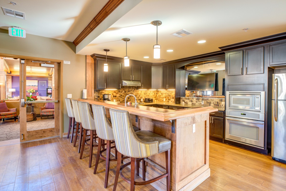 A modern kitchen with a bar counter and comfortable stools, featuring pendant lighting and wood flooring.