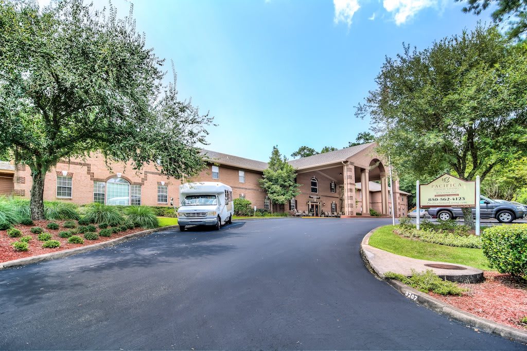 A building with a driveway and a parked van near the entrance, surrounded by trees.
