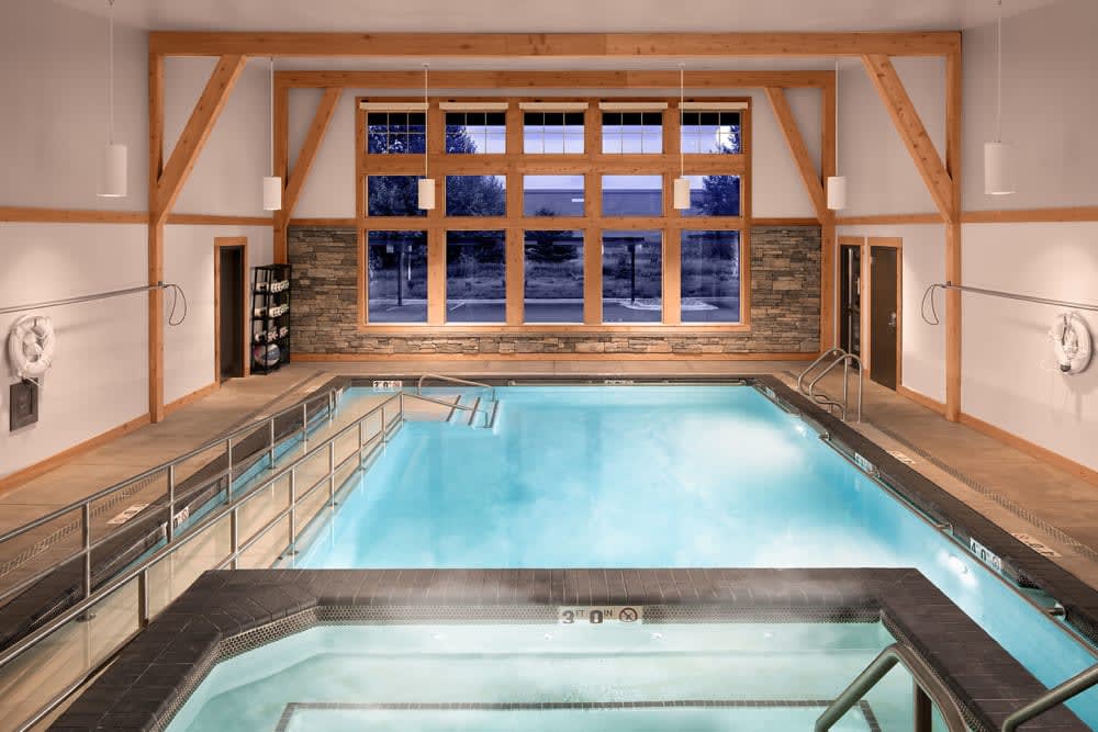 A modern indoor swimming pool with a hot tub, surrounded by large windows.