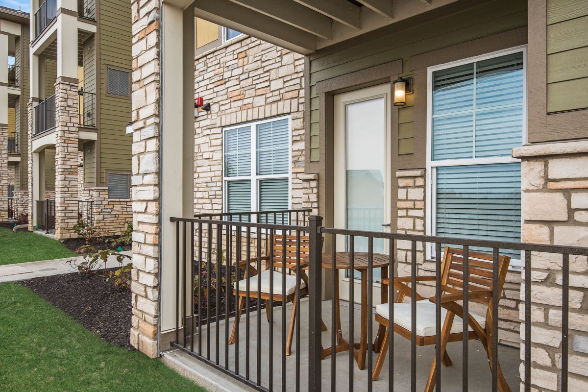 A small outdoor patio with two chairs and a table, enclosed by a black railing against a stone facade.