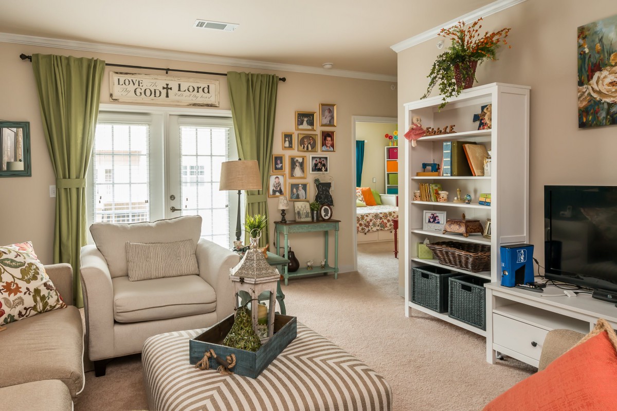 A cozy living room with a comfortable sofa, a bookshelf filled with decor items, and natural light streaming through large windows.