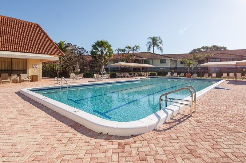 A tranquil outdoor swimming pool surrounded by palm trees at a resort on a sunny day.