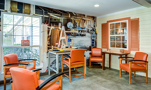 An interior space featuring a workshop-themed mural, with orange chairs and tables arranged for seating.