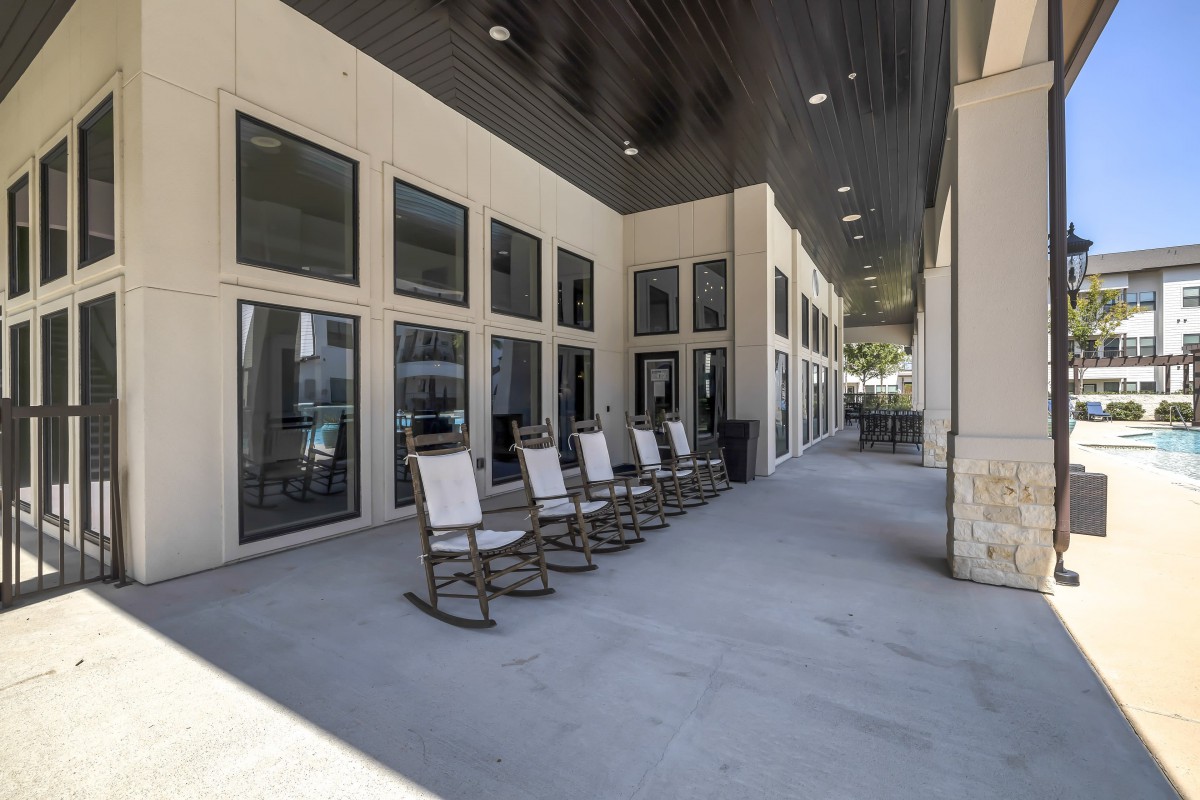A shaded porch with a row of rocking chairs along the side of a building.