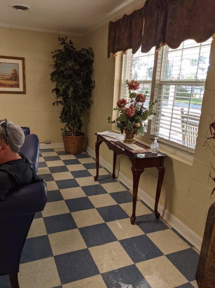 A cozy waiting room with checkered flooring, a window letting in natural light, and a decorative table with flowers.