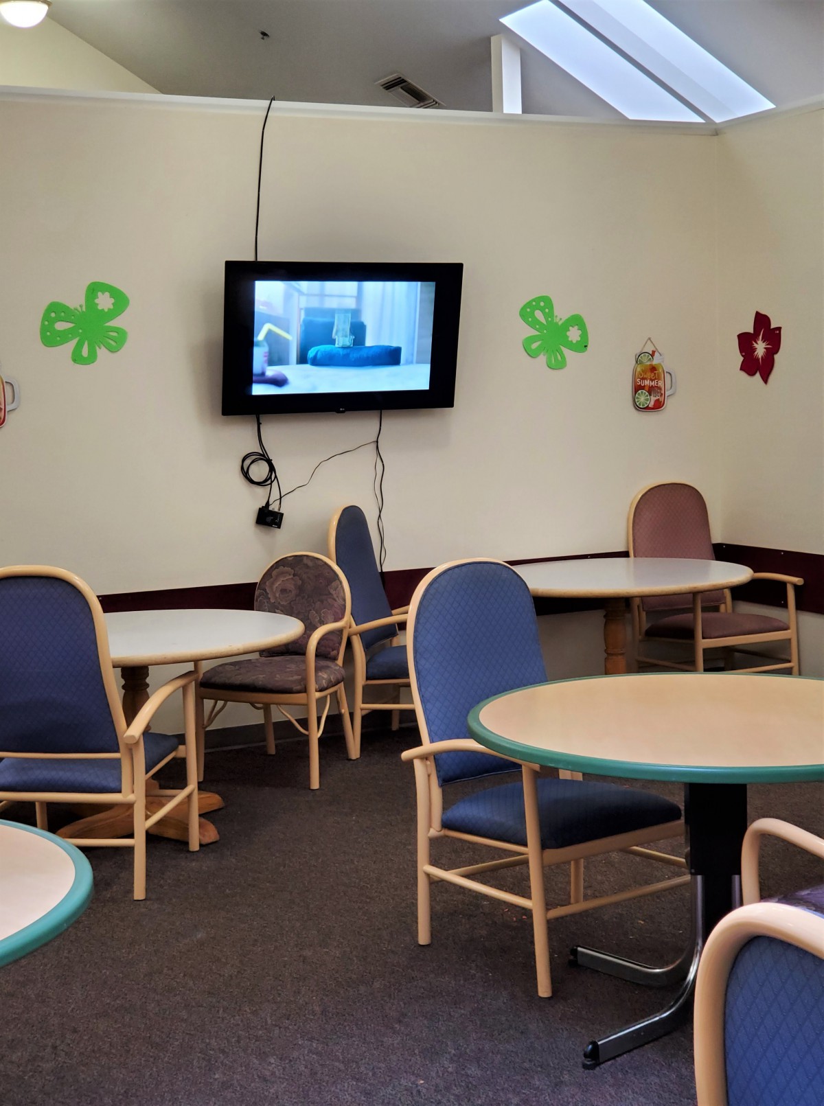 A common area with tables and chairs, featuring a television and wall decorations.