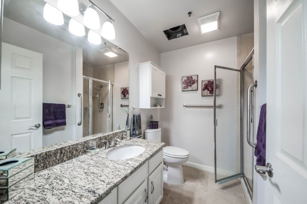 A modern bathroom with granite countertops and a glass-enclosed shower.