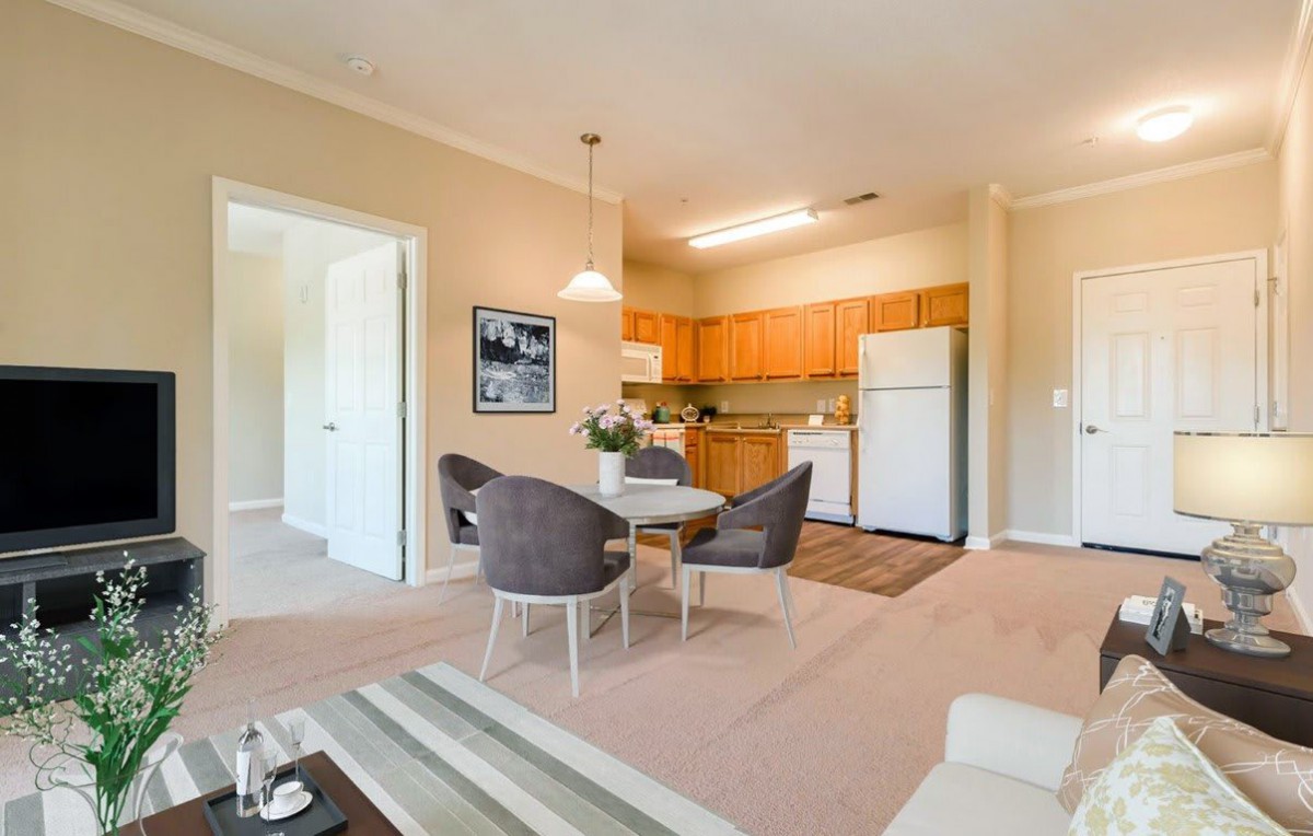 A cozy open-plan living area featuring a small dining set and a kitchen with wooden cabinets.
