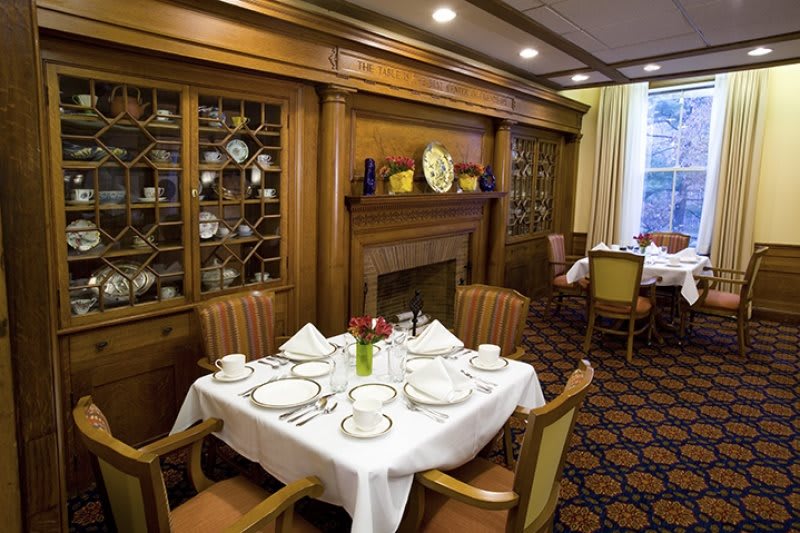 A elegantly set dining table in a traditional dining room with a fireplace and decorative wooden cabinetry.