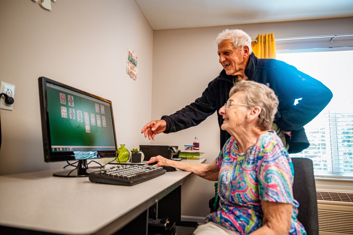 An elderly couple engaging with a computer to play solitaire together.