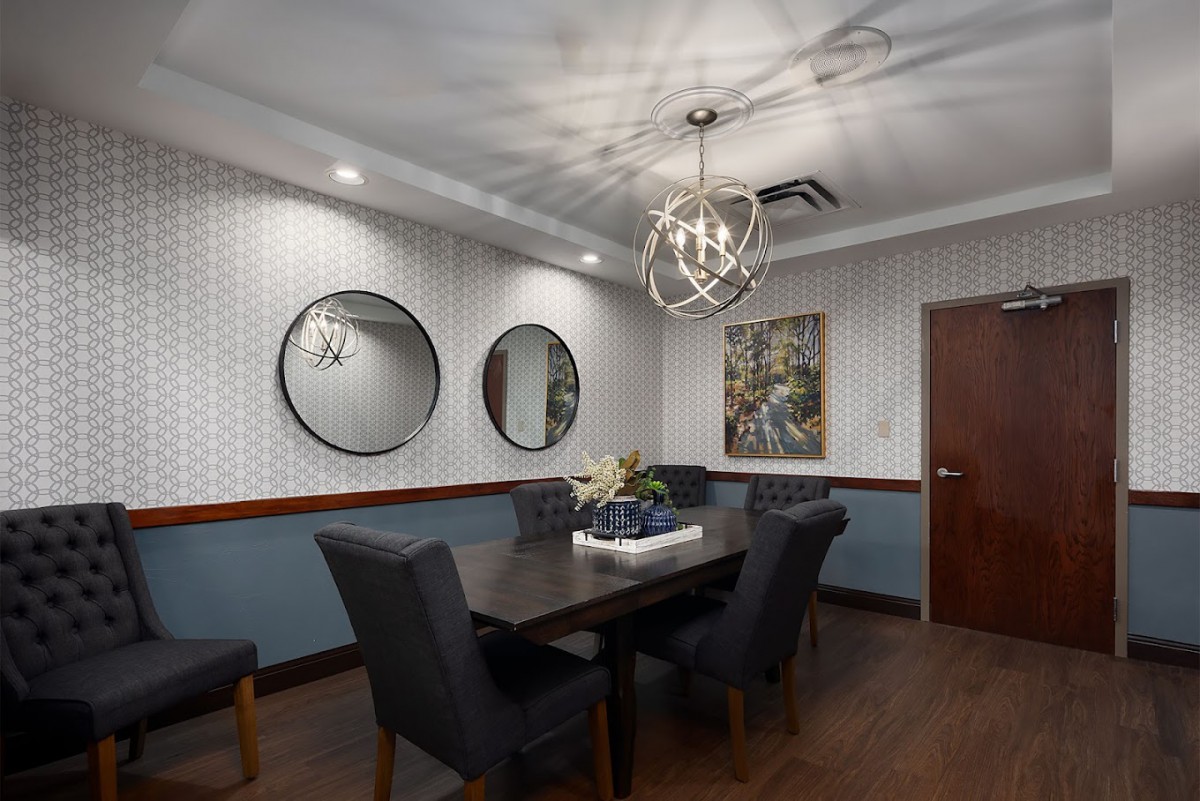 A modern dining room featuring a sleek table and upholstered chairs, with decorative mirrors and artwork adorning the walls.
