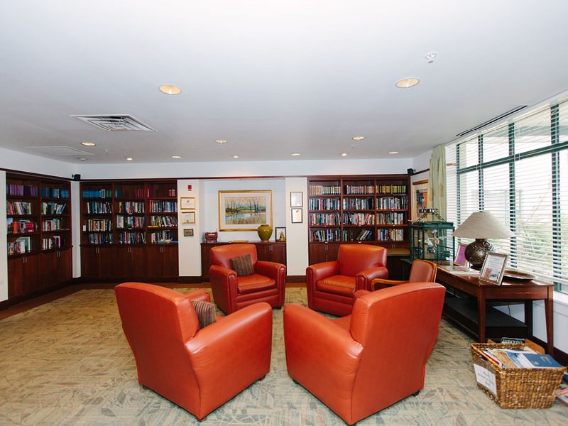 A cozy library room featuring a seating area with red chairs and walls lined with bookshelves.