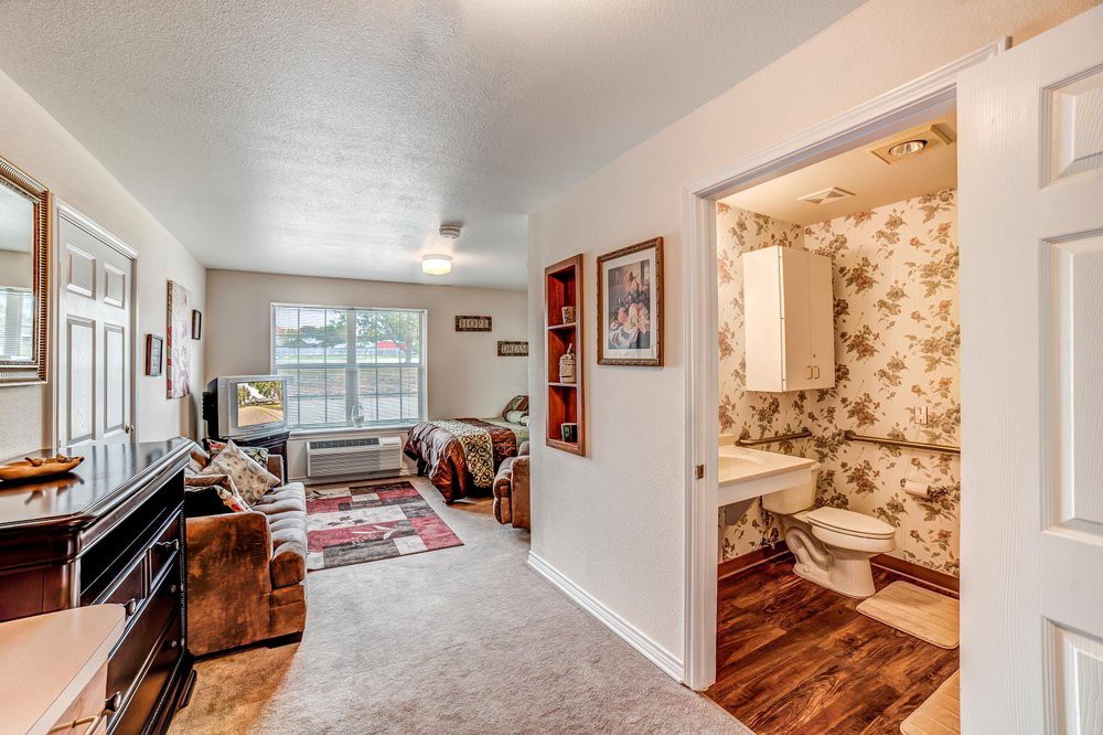 A cozy living room with a sofa, carpet, and adjacent bathroom with floral wallpaper.