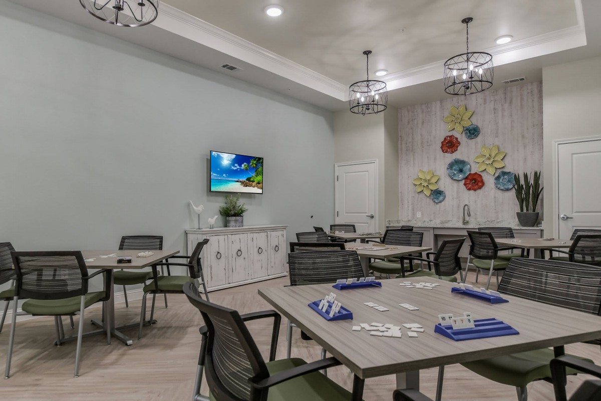 A modern dining room with several tables and chairs, featuring decorative light fixtures, wall art, and a television.